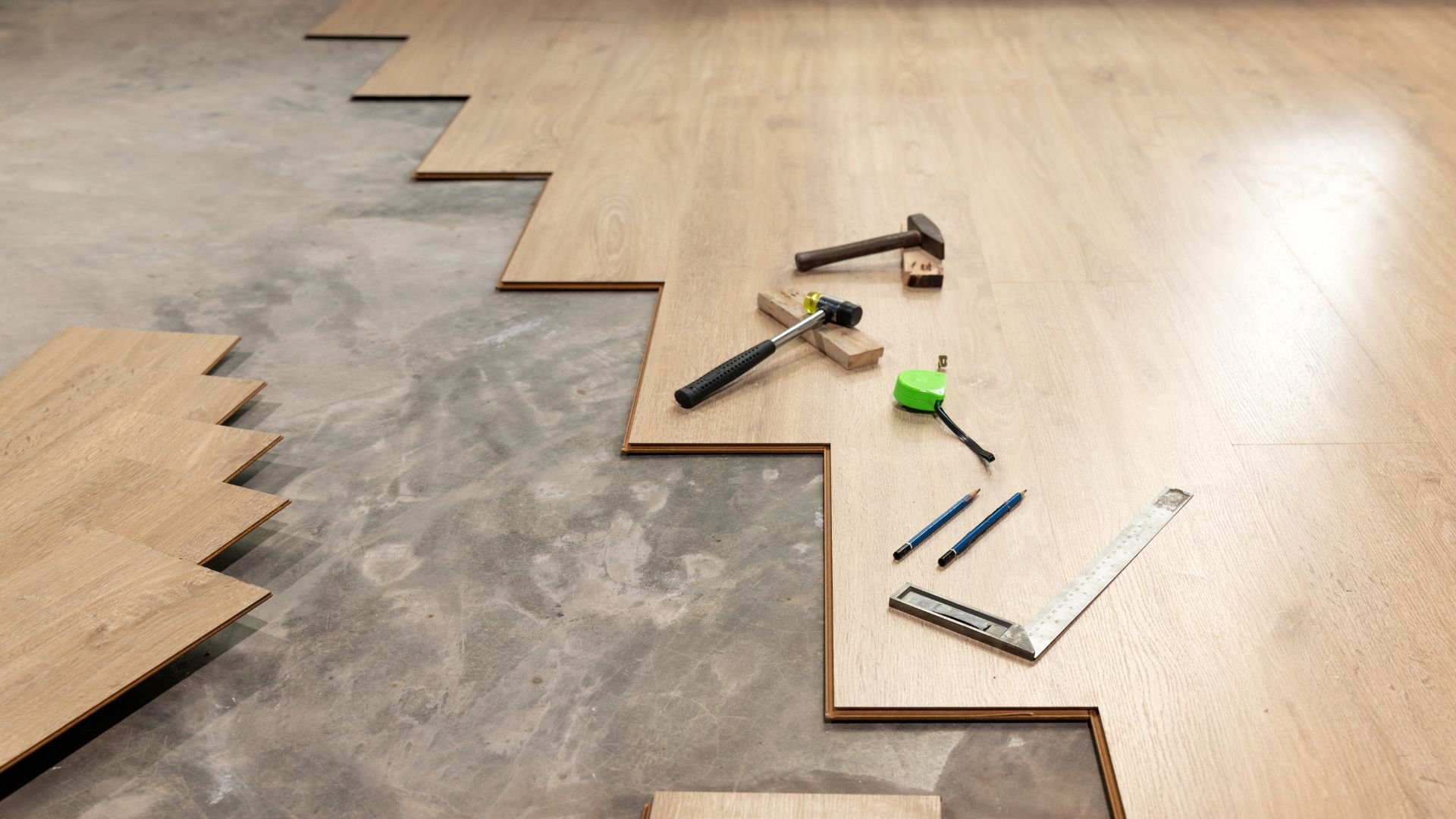 Wooden flooring installation with hammers, measuring tools, and green tape