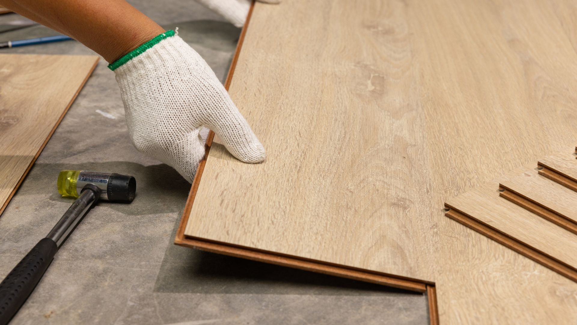 Worker installing laminate flooring with gloved hand and rubber mallet