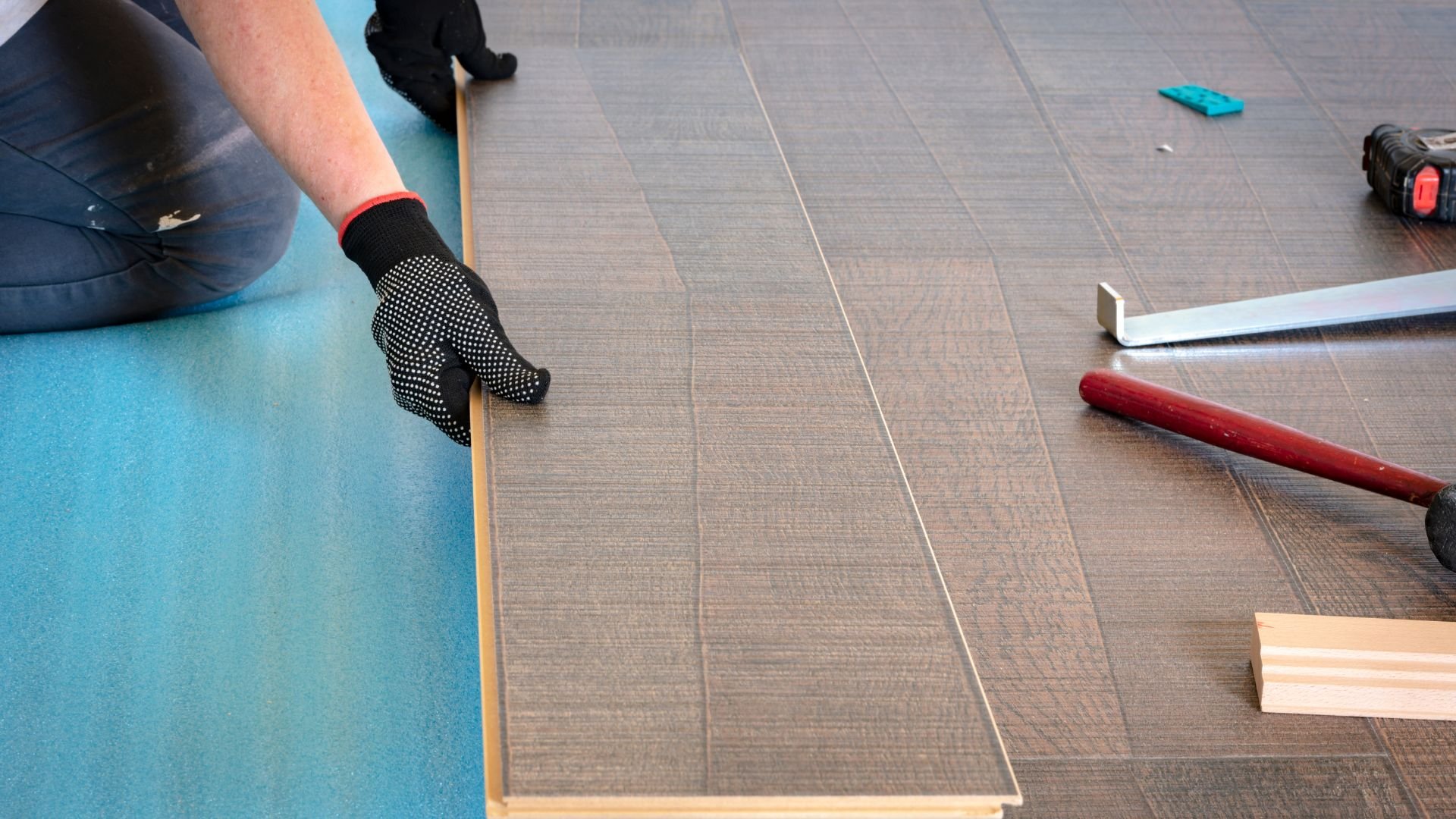 Worker installing wooden laminate flooring with tools nearby